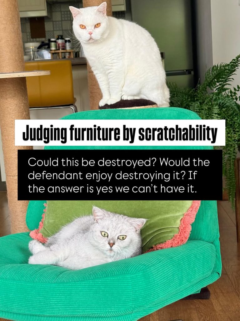 A silver-shaded British Shorthair cat lies relaxed on a bright green corduroy armchair with a pink-fringed green pillow, while a white British Shorthair cat sits perched on a tall sisal scratching post in the background. A black text block overlay reads: "Judging furniture by scratchability Could this be destroyed? Would the defendant enjoy destroying it? If the answer is yes we can’t have it."